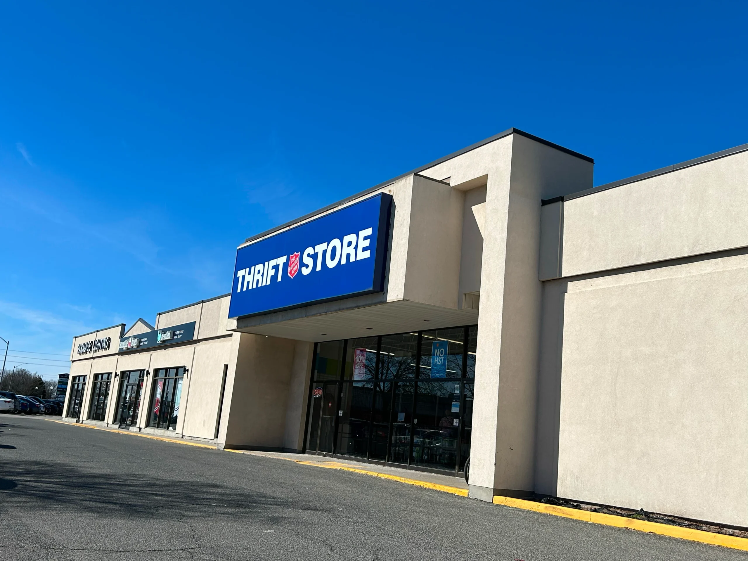 Blue sign reading 'THRIFT STORE' on a beige storefront under a clear blue sky