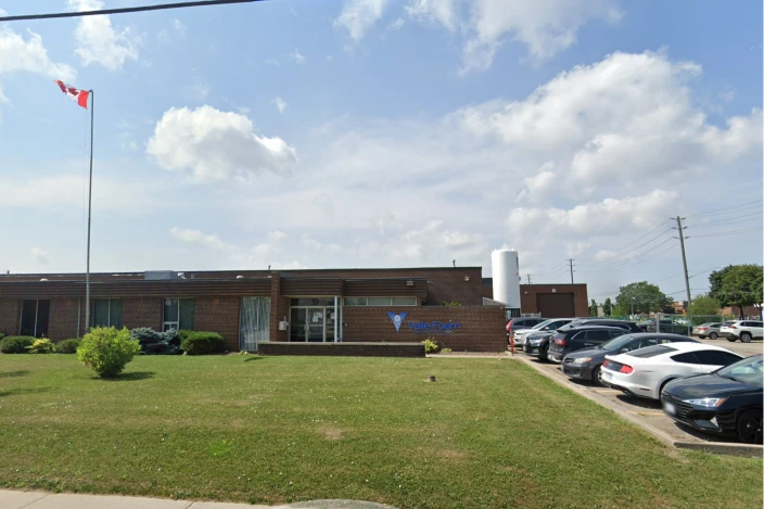 Brick single-story office building with a Canadian flag on a tall pole, a blue ValueForge sign, manicured lawn, and a row of parked cars under a partly cloudy sky.
