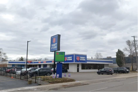 Exterior of a single-story thrift store with blue signage and a parking lot, several cars parked in front.