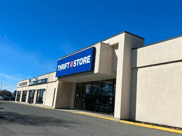 Blue sign reading 'THRIFT STORE' on a beige storefront under a clear blue sky