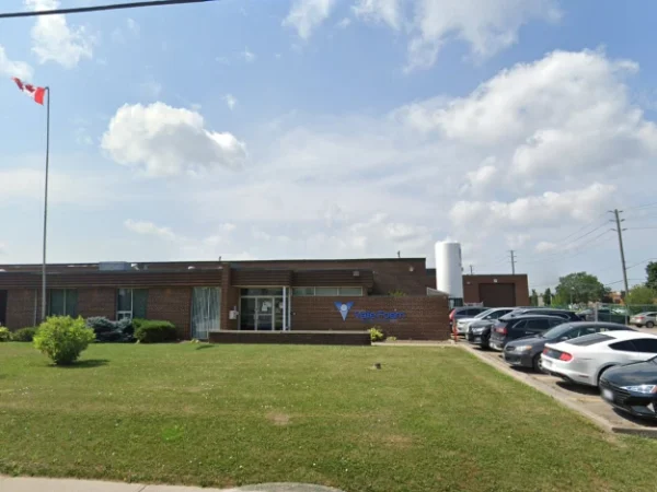 Brick single-story office building with a Canadian flag on a tall pole, a blue ValueForge sign, manicured lawn, and a row of parked cars under a partly cloudy sky.