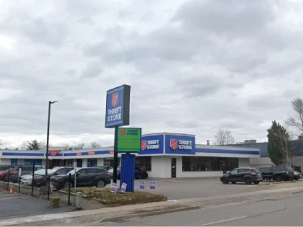 Exterior of a single-story thrift store with blue signage and a parking lot, several cars parked in front.